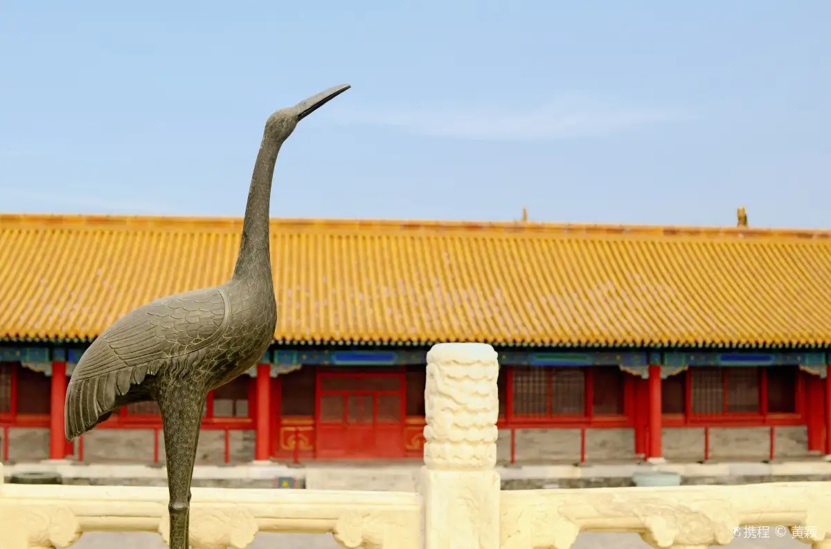 Bronze crane statue in front of golden roofs